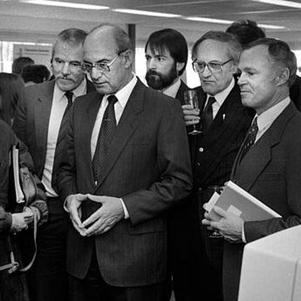 1986: 50 Millionen D-Mark für Lehre und Forschung (Foto: Universitätsarchiv Paderborn) Schwarz-weiß Foto, mehrere Personen stehen versammelt vor einem Computer und schauen diesen an.
