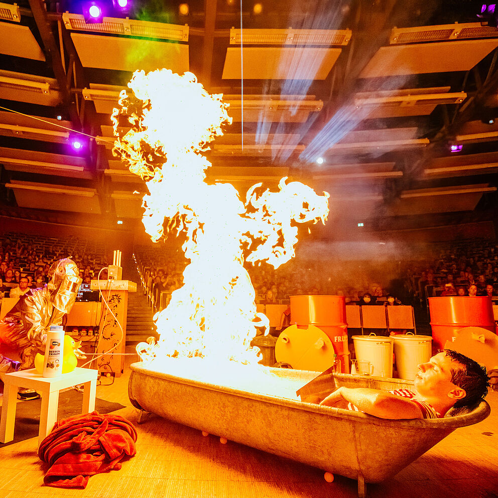 Fynn Bremser nimmt ein entspanntes Bad in der brennenden Badewanne vor Besucher*innen der Event-Physik-Show.