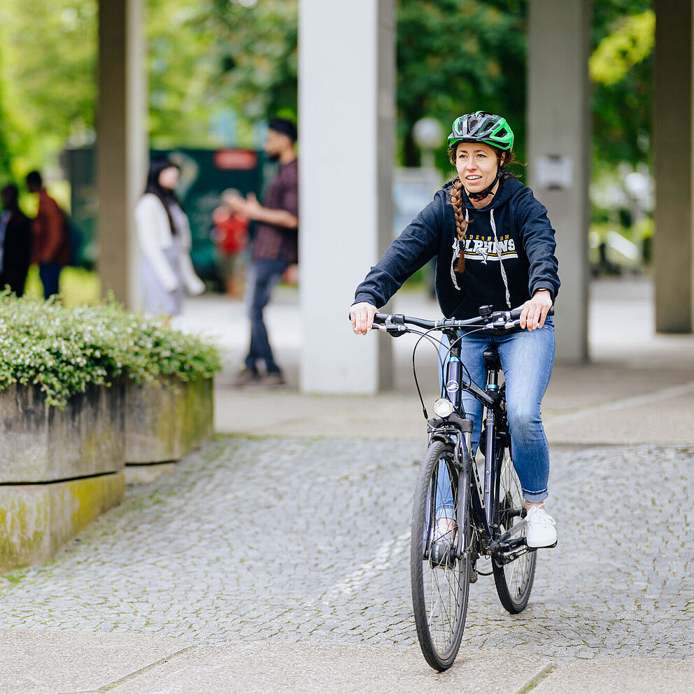 A woman rides her bicycle across the campus of Paderborn University.