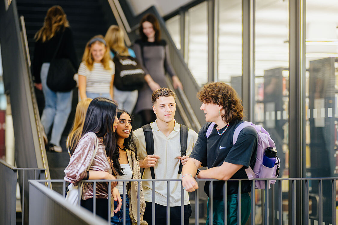 Studierende unterhalten sich am Treppengeländer. 