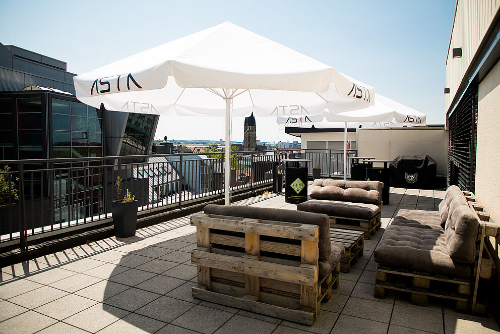 Die Dachterrasse des AStA Stadtcampus in der Paderborner Innenstadt lädt mit Palettenmöbeln und Sonnenschirmen zum Verweilen ein.